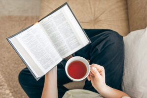 close up young woman drinking hot tea reading favorite paper book top view